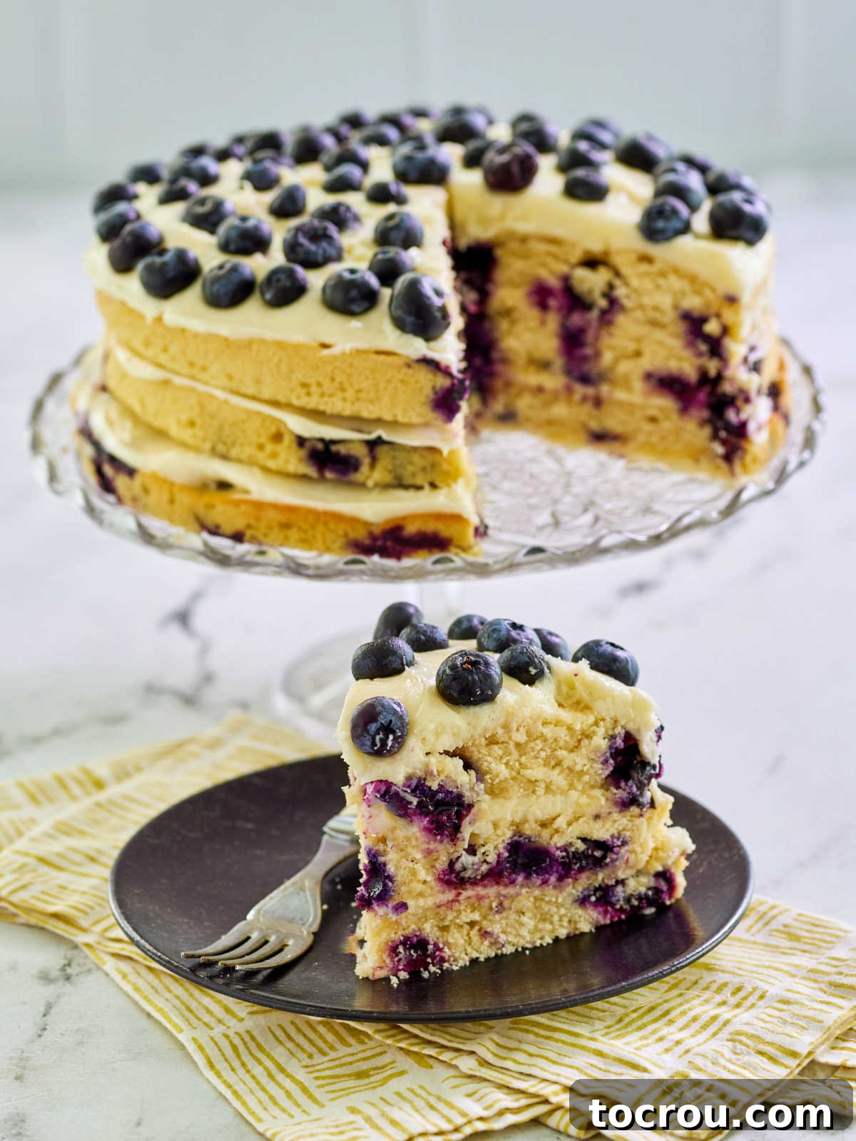A delectable slice of a three-layer lemon blueberry cake, showcasing perfectly baked cake layers interspersed with generous dollops of creamy cream cheese frosting. The slice is ready to be enjoyed, highlighting its moist texture and vibrant fruit.