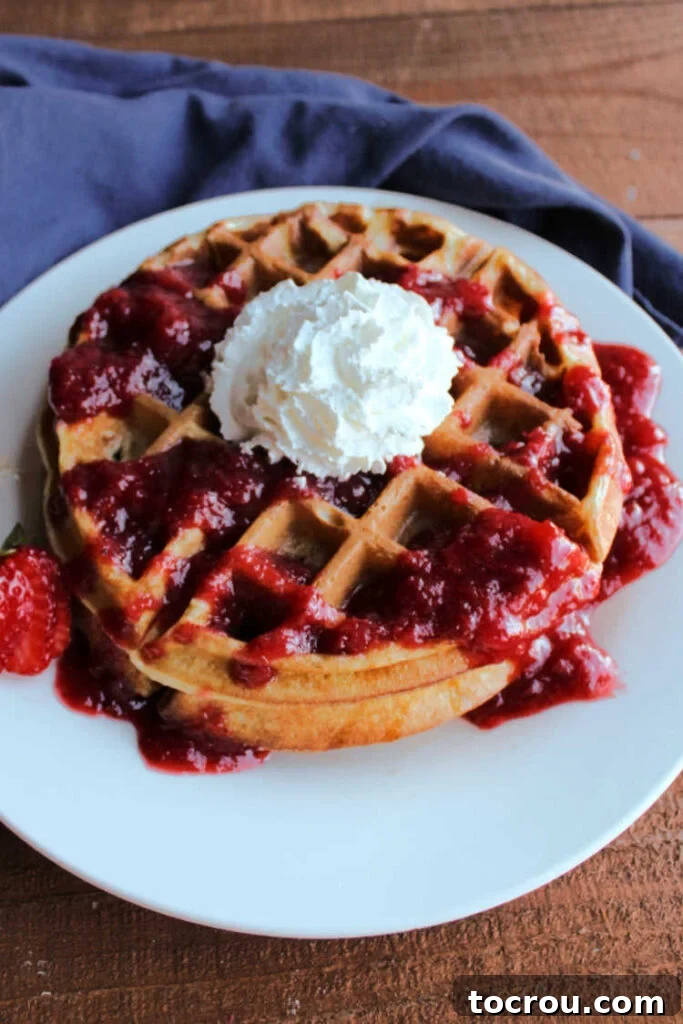 Stack of sourdough waffles generously topped with fresh strawberries and fluffy whipped cream