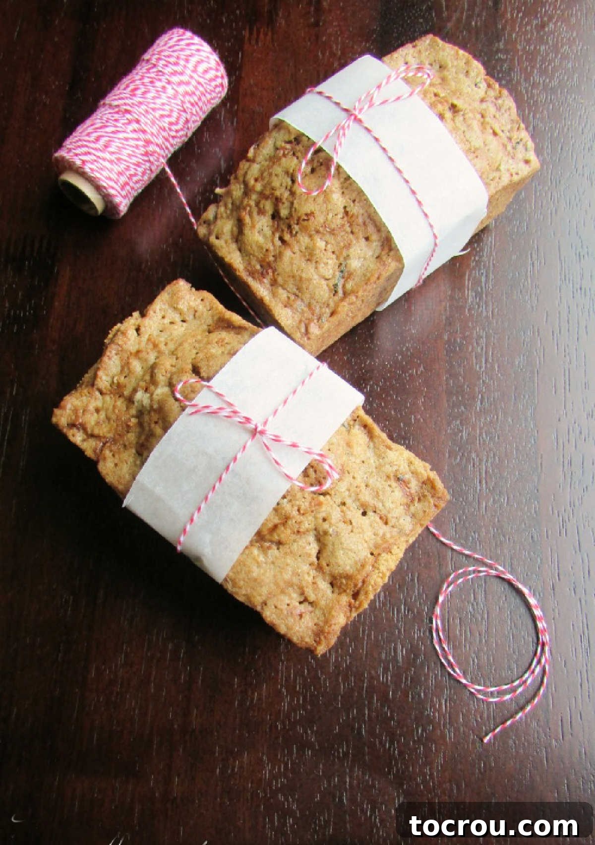 Preparing delicious mini zucchini bread loaves for gifting. Hands tying baker's twine and parchment paper around two mini zucchini bread loaves, preparing them for a gift.