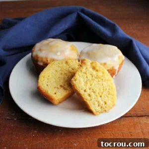 Plate of glazed lemon summer squash muffins with one cut open showing the soft, yellow interior.