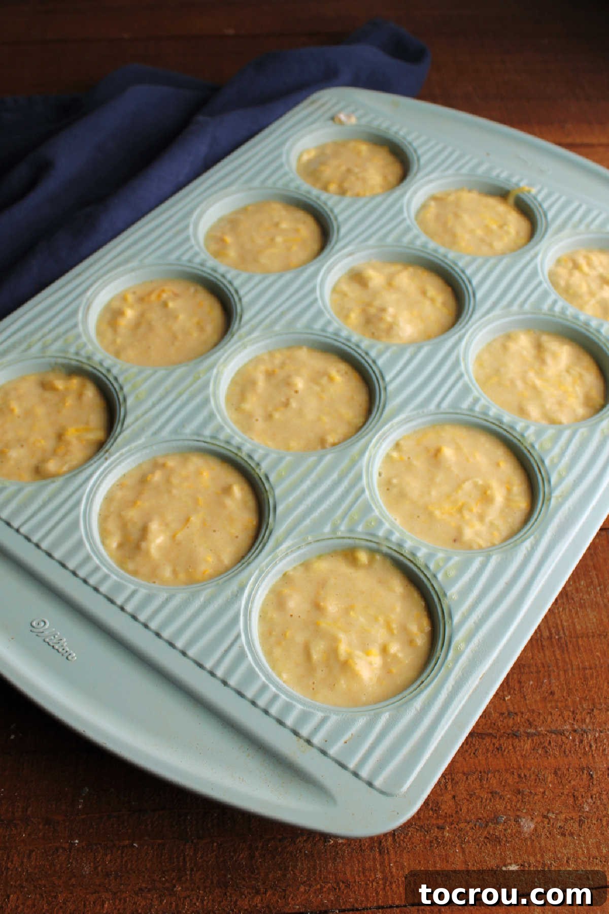 Muffin batter in pan Lemon yellow squash muffin batter spooned into greased muffin pan.
