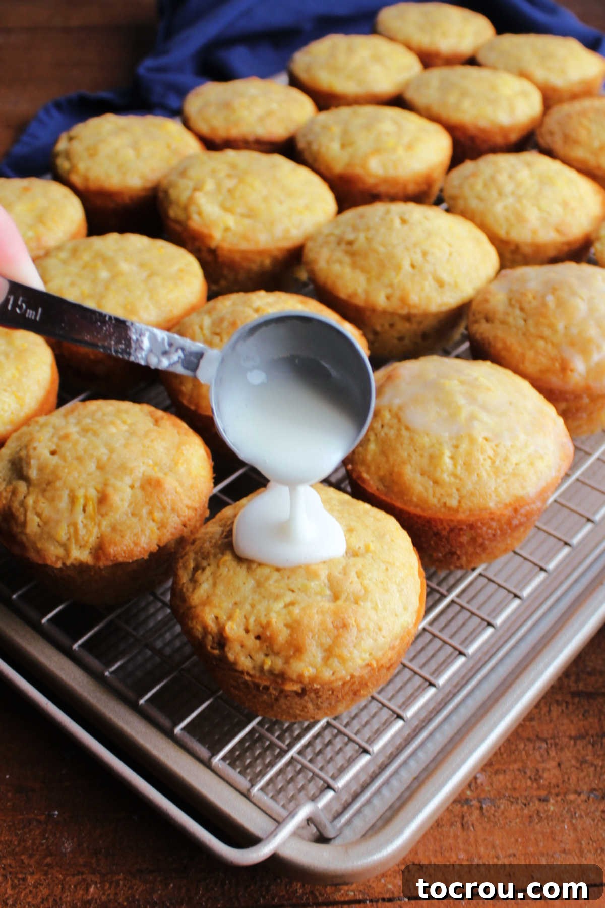 Glazing a muffin Spooning lemon glaze on top of hot lemon summer squash muffin on wire cooling rack.