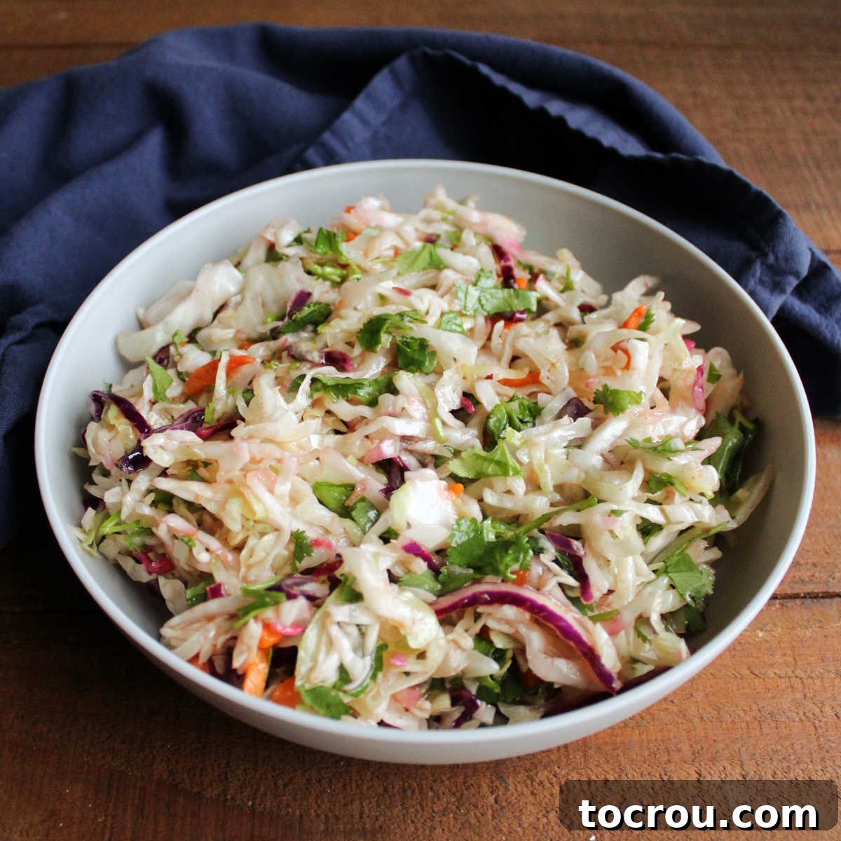 This Honey Lime Slaw with Cilantro and Sriracha is a fresh and fun side dish. It is also great on Asian inspired tacos. Delish! Serving bowl filled with vibrant honey lime slaw dressed with homemade dressing, fresh cilantro, and a drizzle of sriracha, ready to be enjoyed.