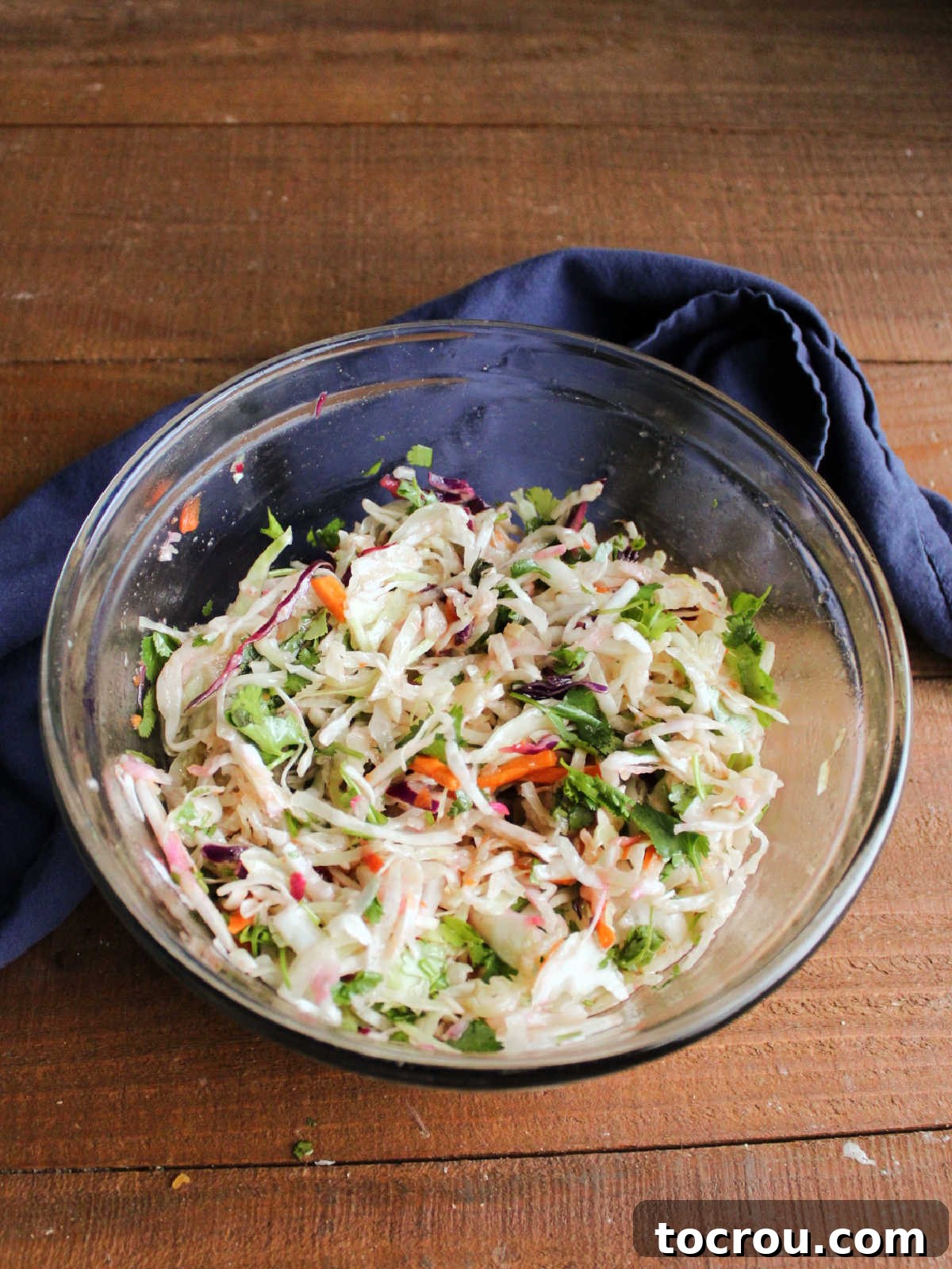 The honey lime slaw is perfectly mixed with cilantro, ready to be served. Mixing bowl filled with vibrant honey lime slaw, showing the chopped cilantro thoroughly mixed in, highlighting the uniform coating of the dressing on the shredded vegetables.