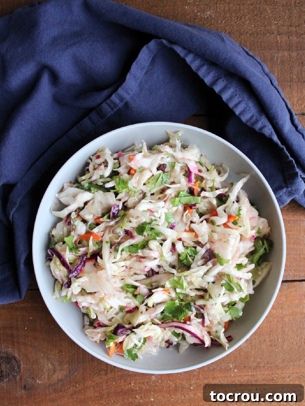 A serving bowl of the finished Honey Lime Slaw, looking fresh and appetizing. Elegant gray serving bowl filled with zesty honey lime slaw, garnished with fresh cilantro and a hint of sriracha, showcasing its readiness for a meal.