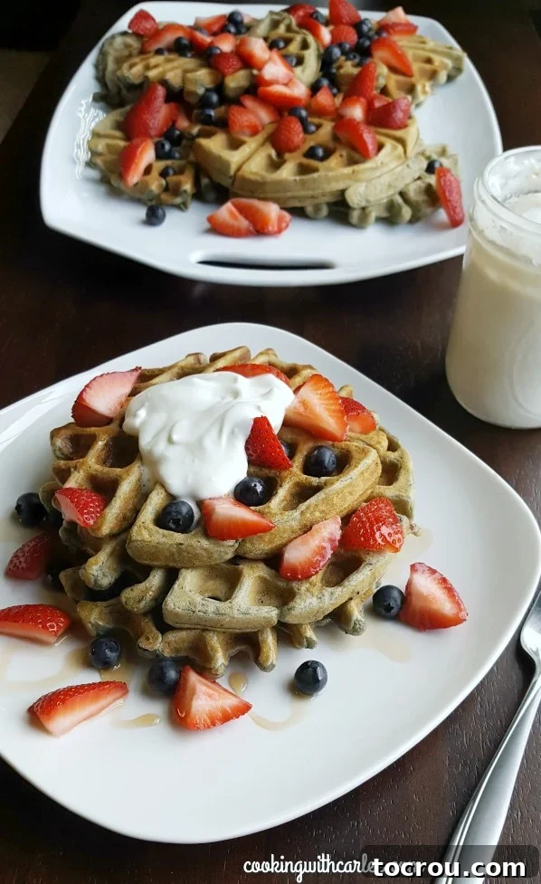 Blueberry Sourdough Waffles: Serve with strawberries and maple whipped cream for a patriotic treat or simply with syrup for a weekend delight! A charming plate featuring blueberry sourdough waffles adorned with fresh strawberries and a luscious maple whipped cream. In the background, a jar of maple whipped cream and a platter of additional waffles hint at a delightful spread.