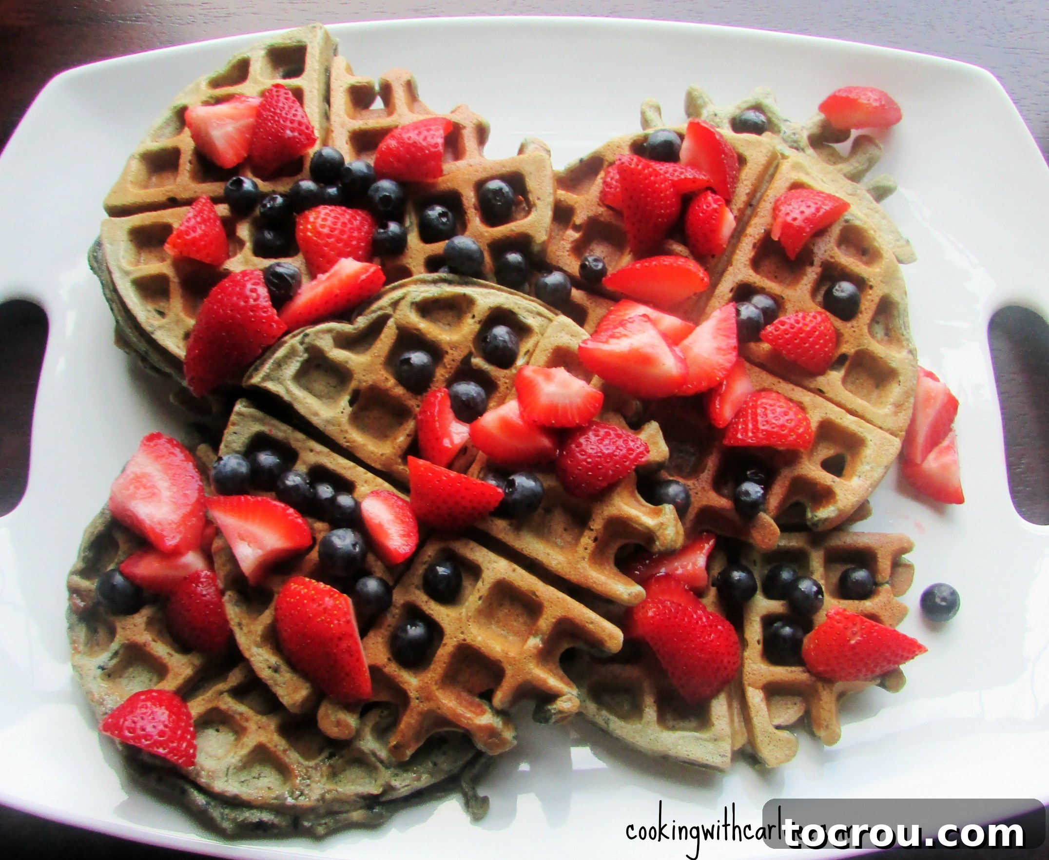 Blueberry Sourdough Waffles: A fantastic way to use sourdough starter discard for a delicious breakfast or brunch. A generous platter filled with freshly made blueberry sourdough waffles, artfully garnished with additional fresh blueberries and pieces of ripe strawberries, showcasing their delicious appeal.