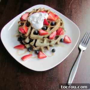 Stack of blueberry sourdough waffles topped with fresh blueberries, strawberries, maple syrup, and whipped cream, ready to eat.