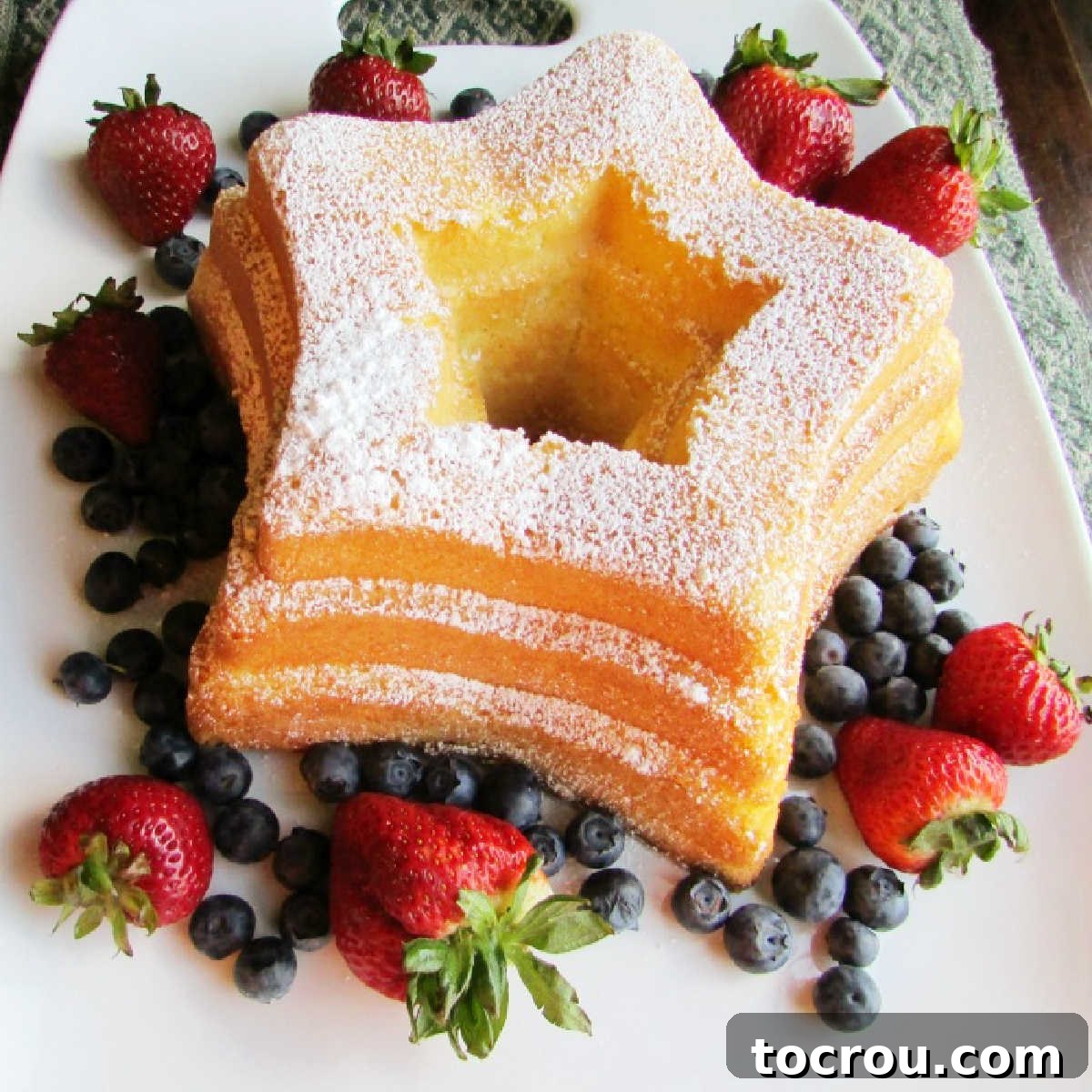 Star shaped sand torte cake dusted with powdered sugar and surrounded with strawberries and blueberries.