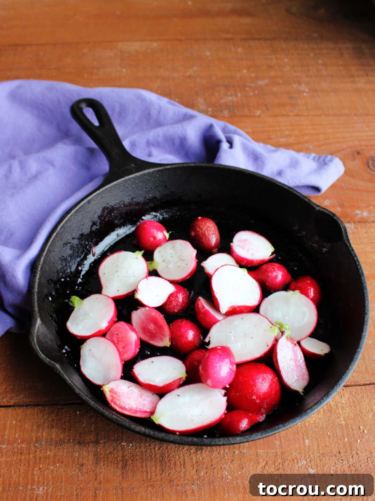 Cast iron skillet with radishes coated in oil, salt, and pepper, ready to roast. 