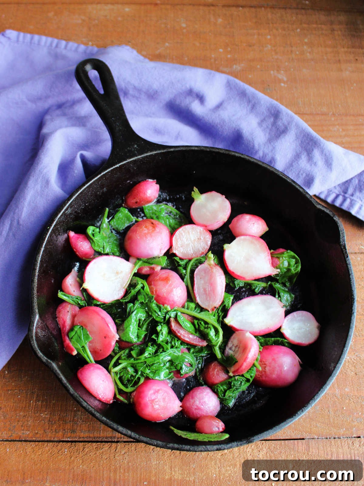 Cast iron skillet with roasted radishes and wilted radish greens coated in a little bit of melted butter, ready to serve. 