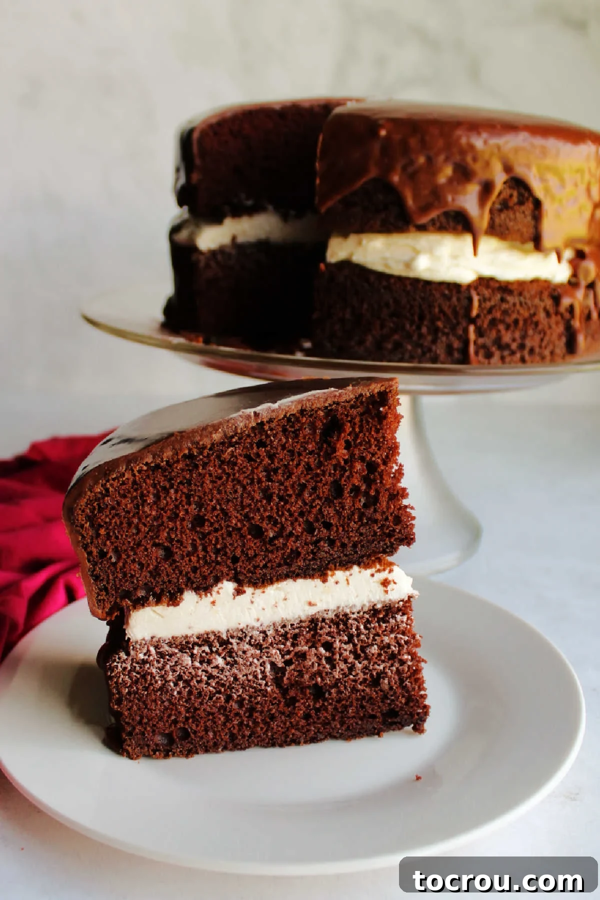 Chocolate Fudge Cream Delight 3 A perfectly portioned slice of Ding Dong cake resting on a plate, featuring a thick layer of fluffy white cream filling sandwiched between two rich chocolate cake layers, all covered in a smooth chocolate icing. The remaining cake sits elegantly in the background.