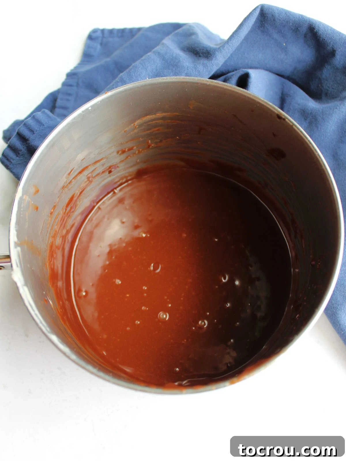 Chocolate Fudge Cream Delight 7 Smooth, dark chocolate icing in a saucepan, glistening and ready to be poured over a cake. The consistency appears perfectly pourable and rich.