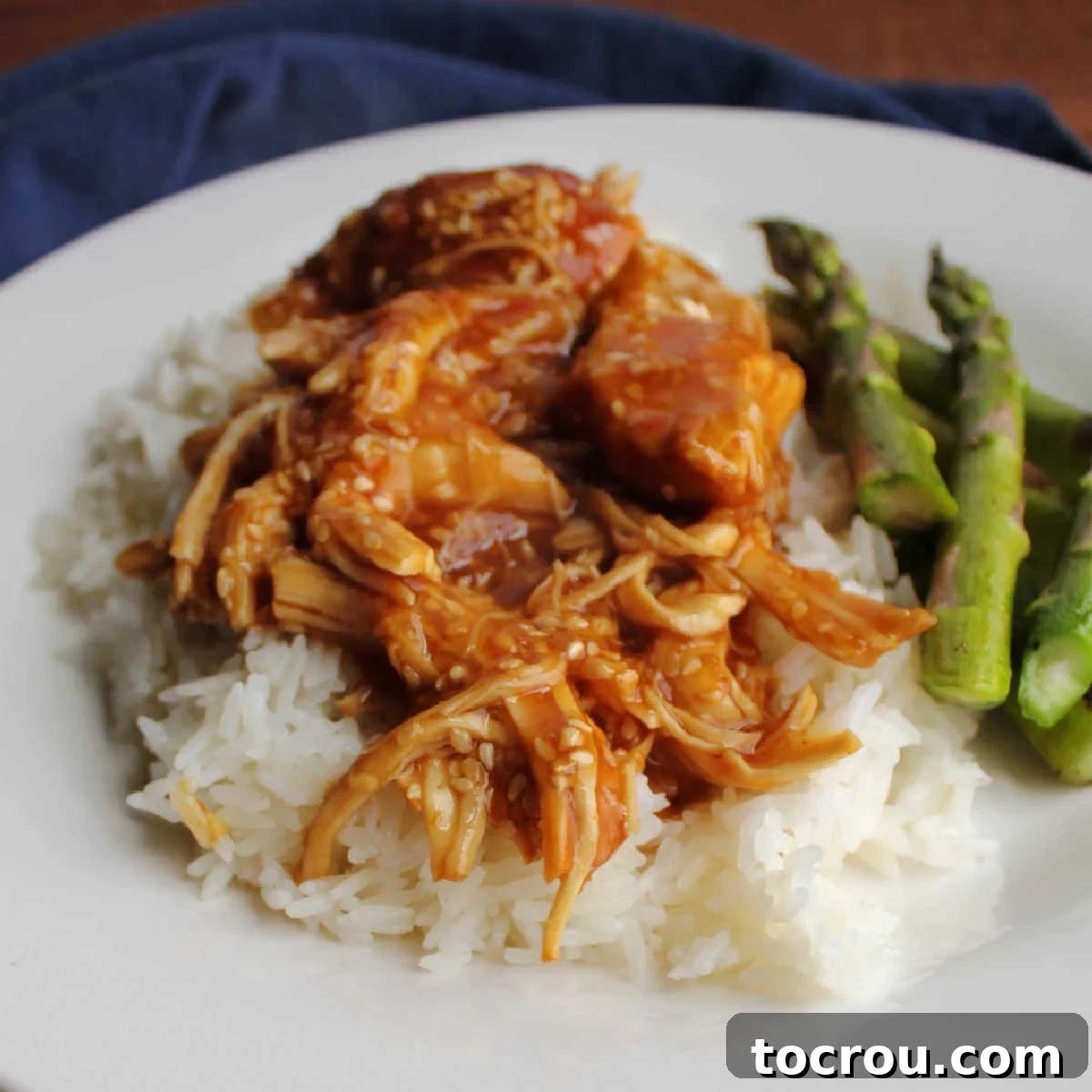 Close up of rice topped with tender, glistening chunks of slow cooker honey sesame chicken, garnished with fresh green onions and toasted sesame seeds for a vibrant finish.