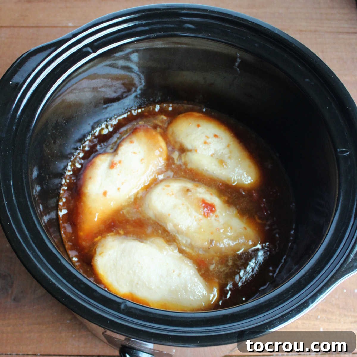 Perfectly cooked whole chicken breasts submerged in a thick, amber-colored honey sesame sauce within the crockpot after slow cooking.
