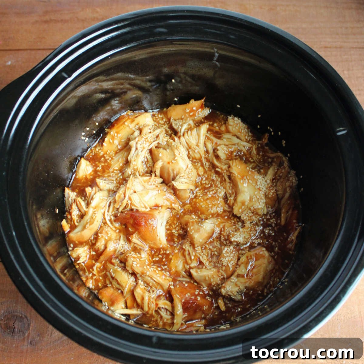 Close-up of lightly shredded chunks of tender chicken coated in a rich, thick honey sesame sauce directly in the slow cooker.