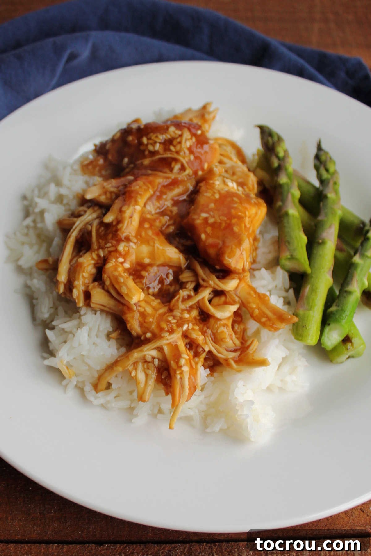 Close-up of sticky honey sesame chicken served on a bed of fluffy white rice, garnished with sesame seeds and chopped green onions.