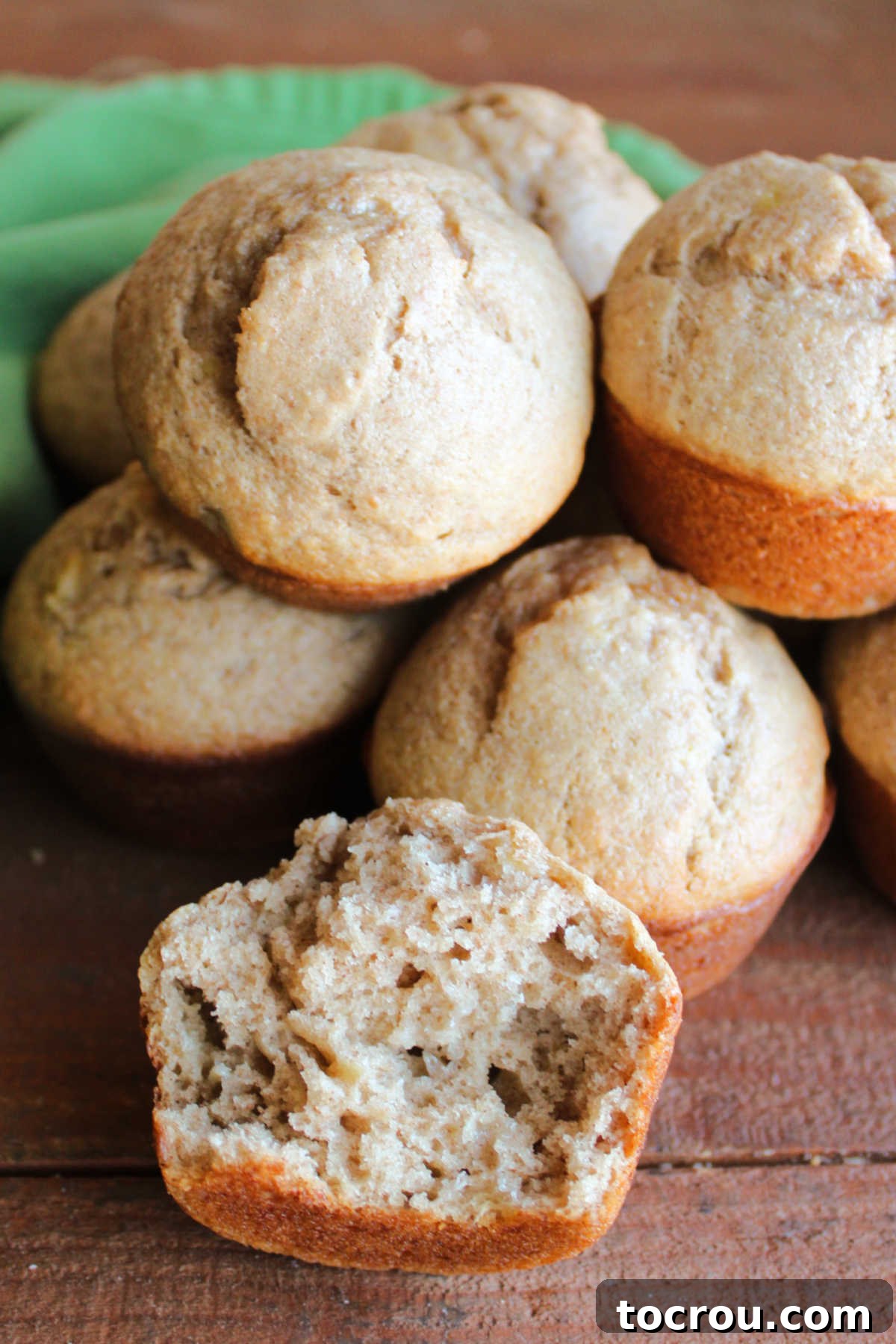 Tangy Sourdough Banana Muffins 3 Pile of sourdough banana bread muffins with one broken open showing its soft interior with bits of banana, flecks of cinnamon, and airy texture.