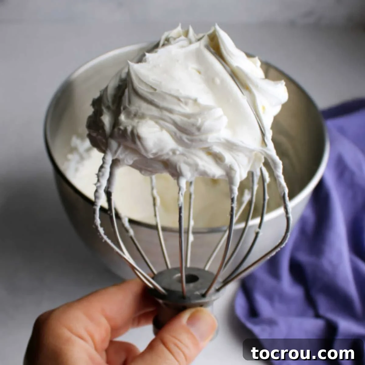 Perfectly Whipped Cream Cheese Topping Balloon whisk attachment from mixer filled with fluffy cream cheese whipped cream.