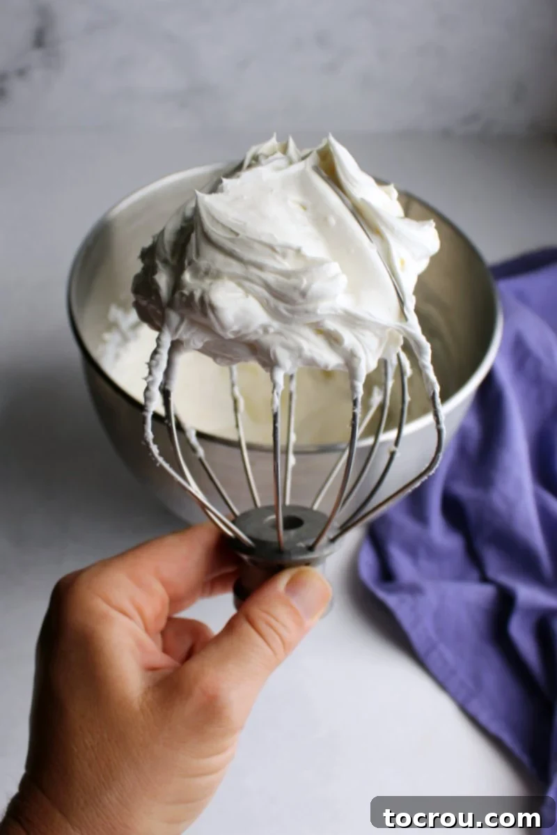 Whisk with Perfect Cream Cheese Whipped Cream hand holding beater full of cream cheese whipped cream