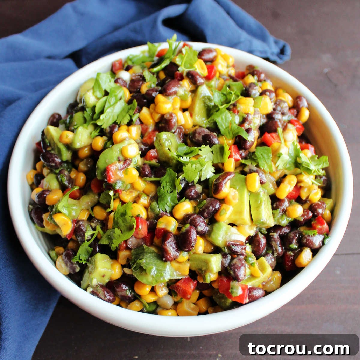 White serving bowl filled with black bean salsa with corn, red pepper, avocado and herbs.