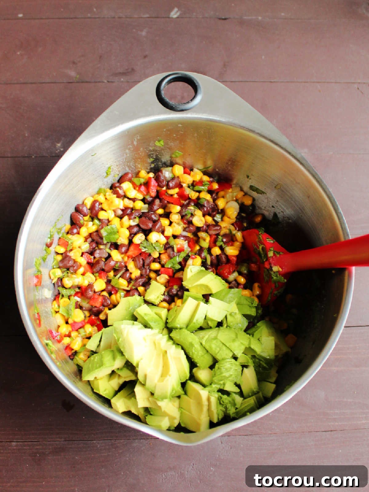 Stirring avocado into black bean salad.