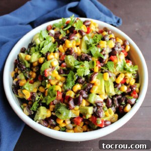 White serving bowl filled with black bean salsa with corn, red pepper, avocado and herbs.