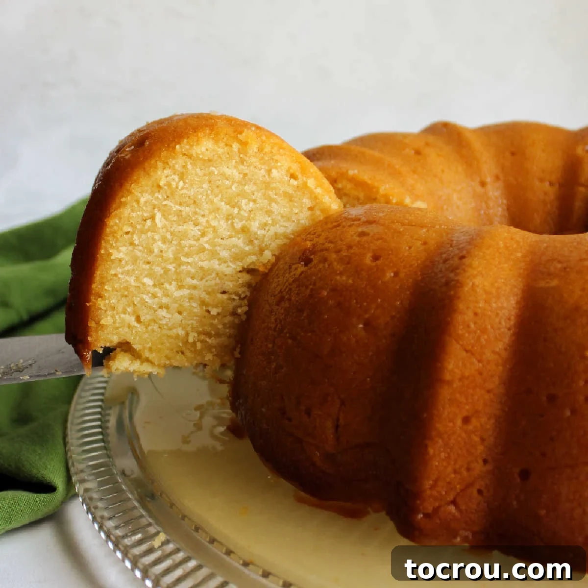 Lifting a slice of honey lemon bundt cake, showcasing its moist texture and golden hue, with the full cake in the background.