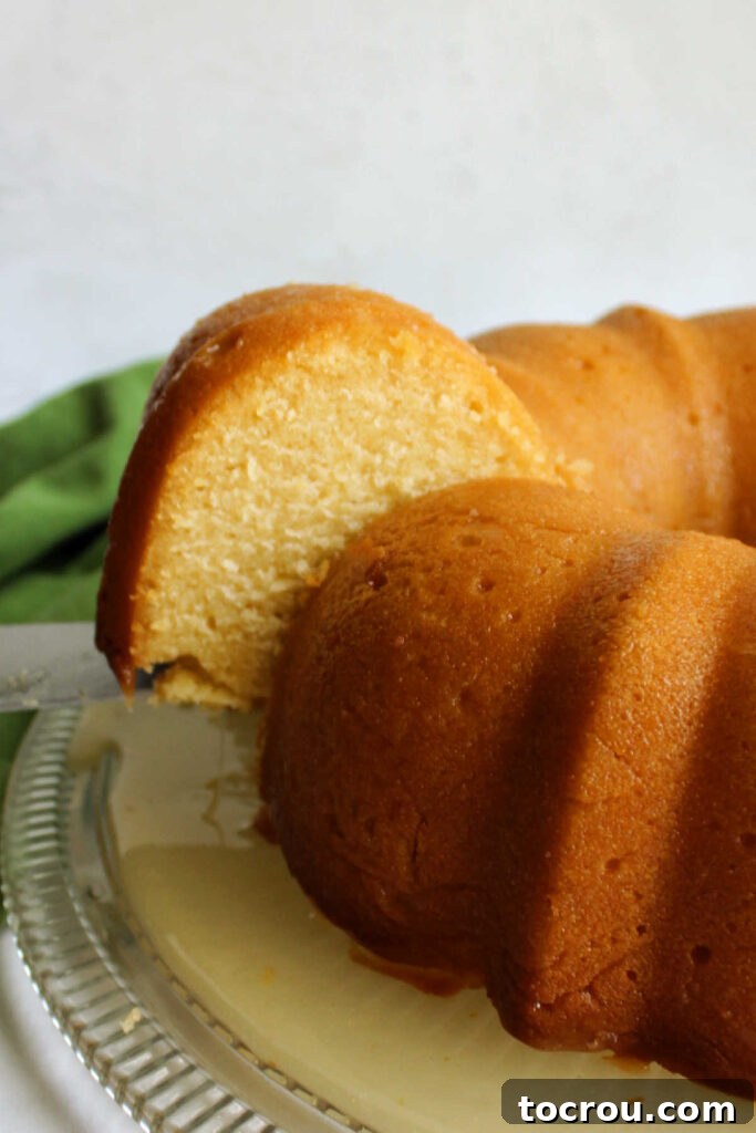 Spatula gently lifting a slice of dense, moist honey lemon bundt cake off a pristine cake plate, highlighting its rich texture.