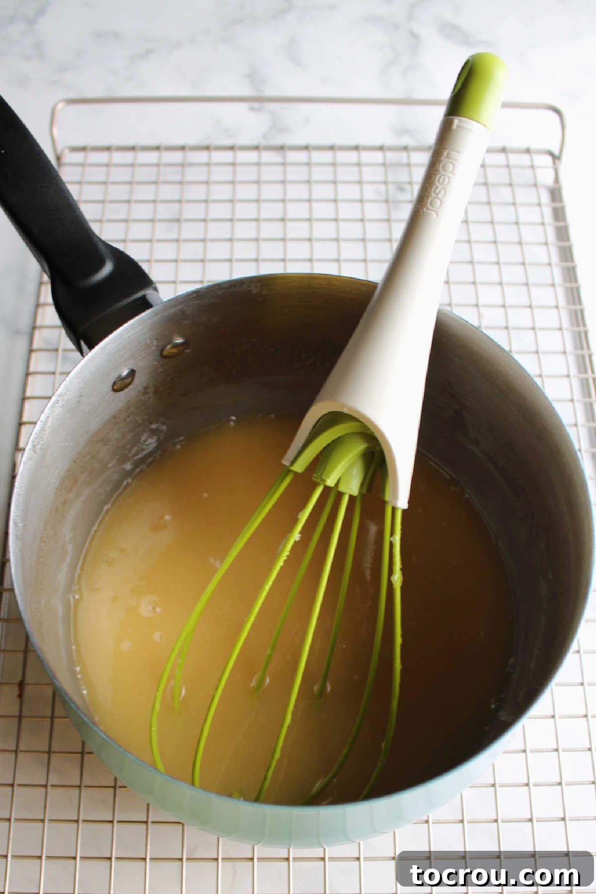 Saucepan containing a rich, golden caramelized honey glaze, with a whisk resting inside, ready for final touches.