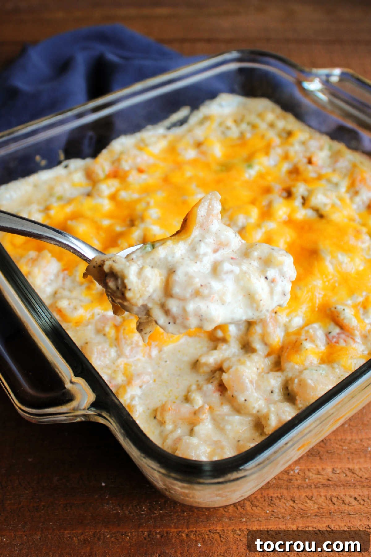 A serving spoon carefully lifts a generous portion of hot, cheesy Cajun shrimp dip from a baking dish.