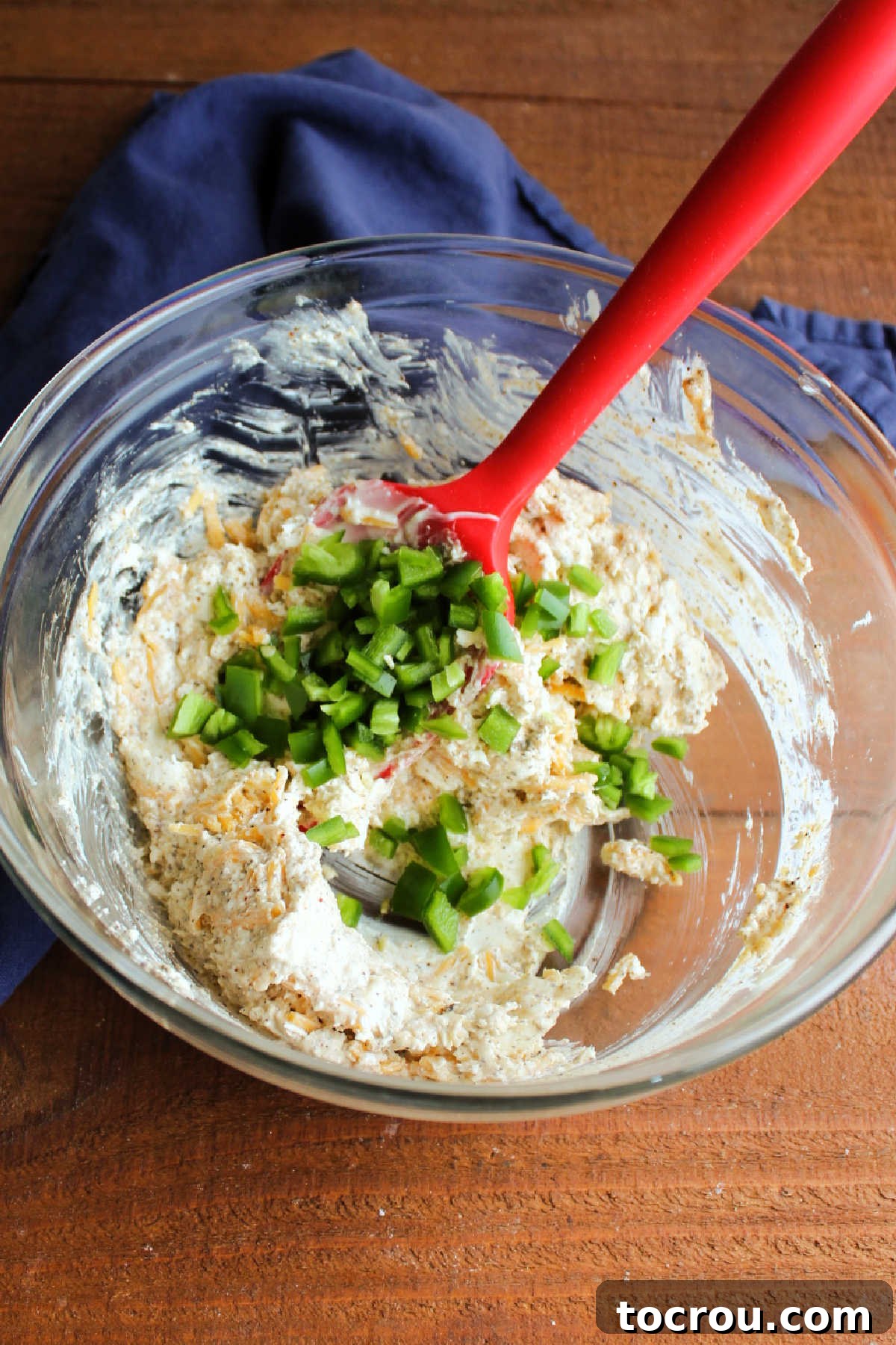 Close-up of diced jalapeño being stirred into a creamy mixture of cream cheese and mayonnaise, ready for the shrimp.