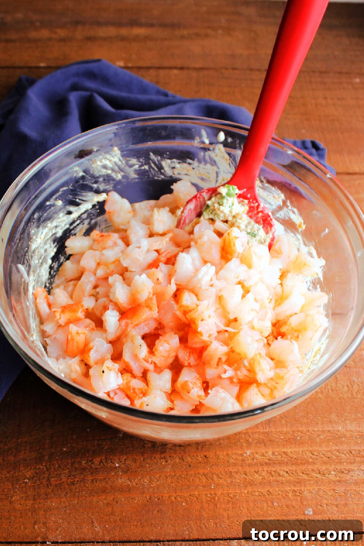 Large, succulent chunks of chopped shrimp being added to a bowl with a creamy, spiced cheese mixture, ready for mixing.