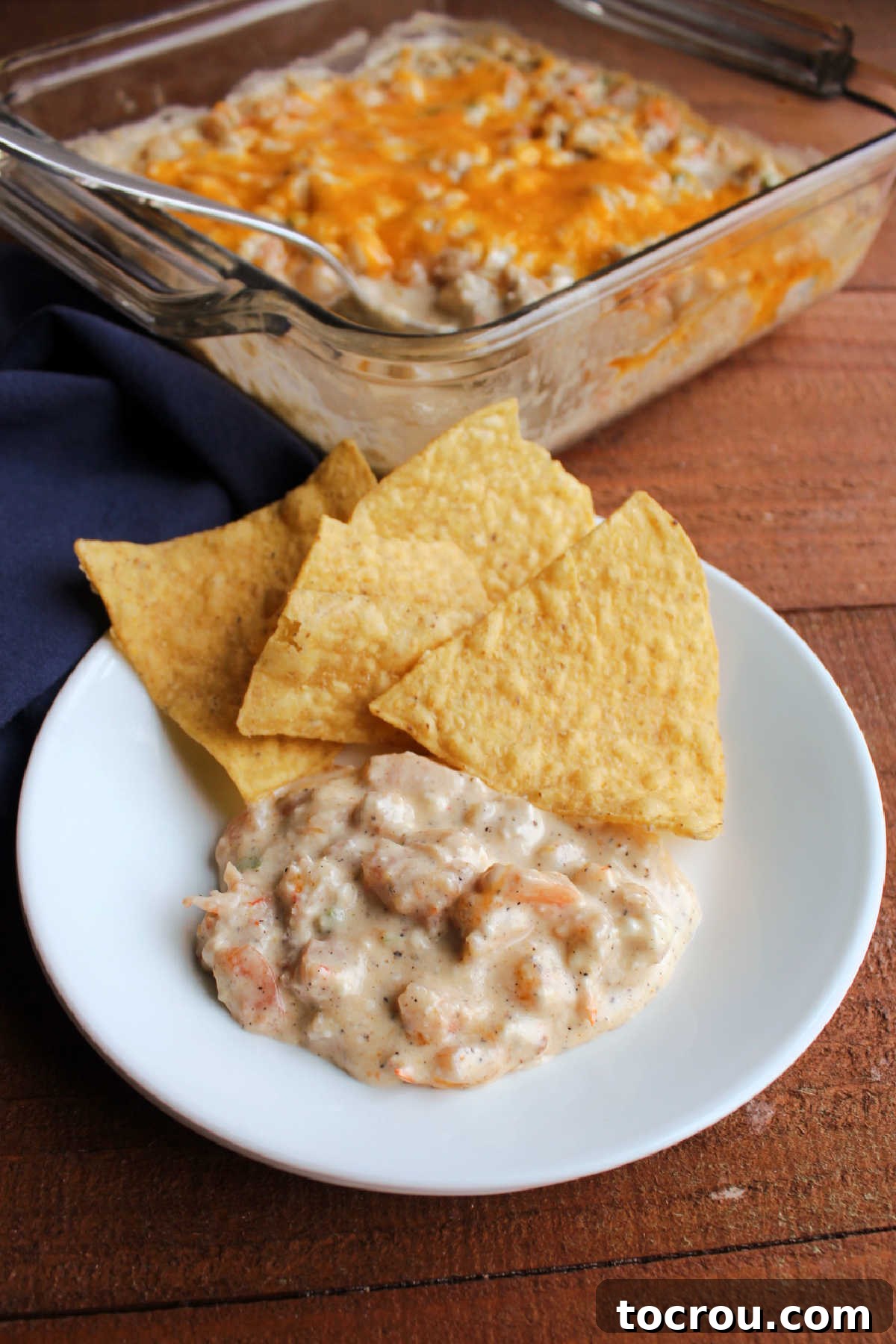 A small plate showcasing a serving of cheesy Cajun shrimp dip, accompanied by crispy tortilla chips, perfect for dipping.