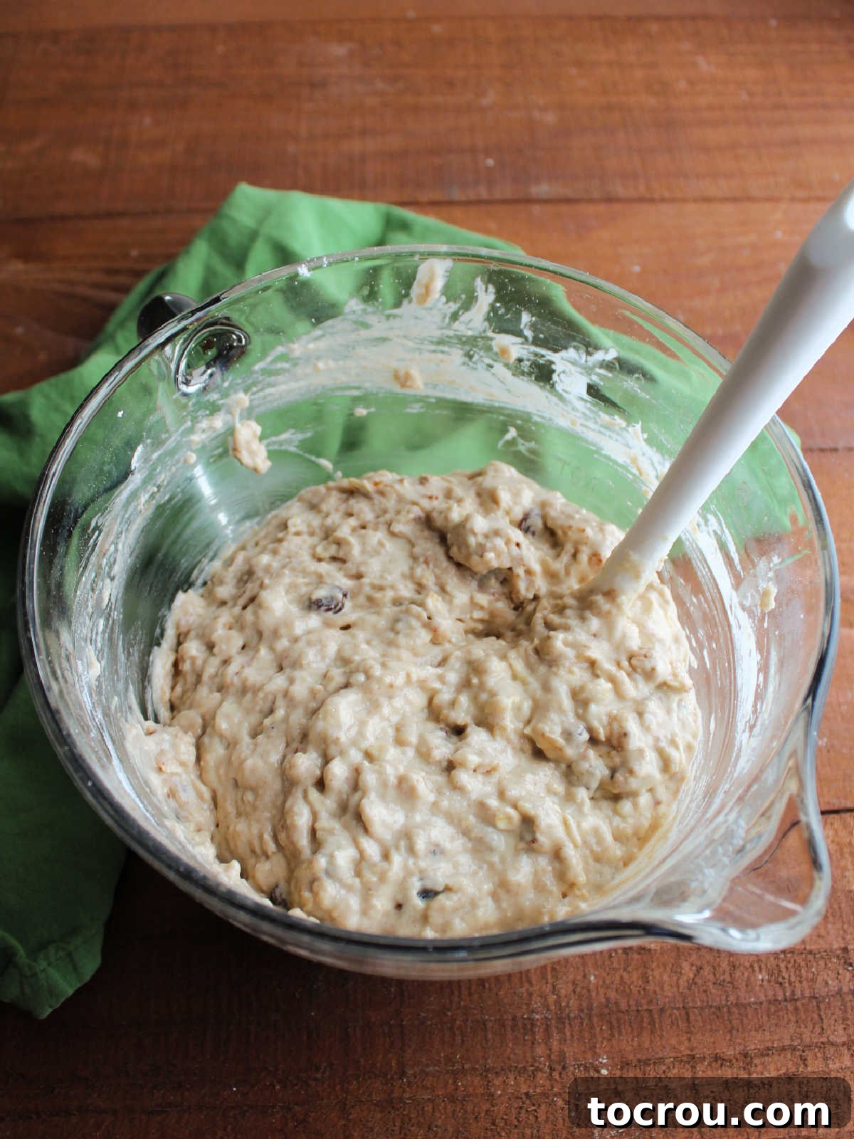 A mixing bowl filled with oatmeal sourdough muffin batter, generously dotted with plump raisins, ready for baking.
