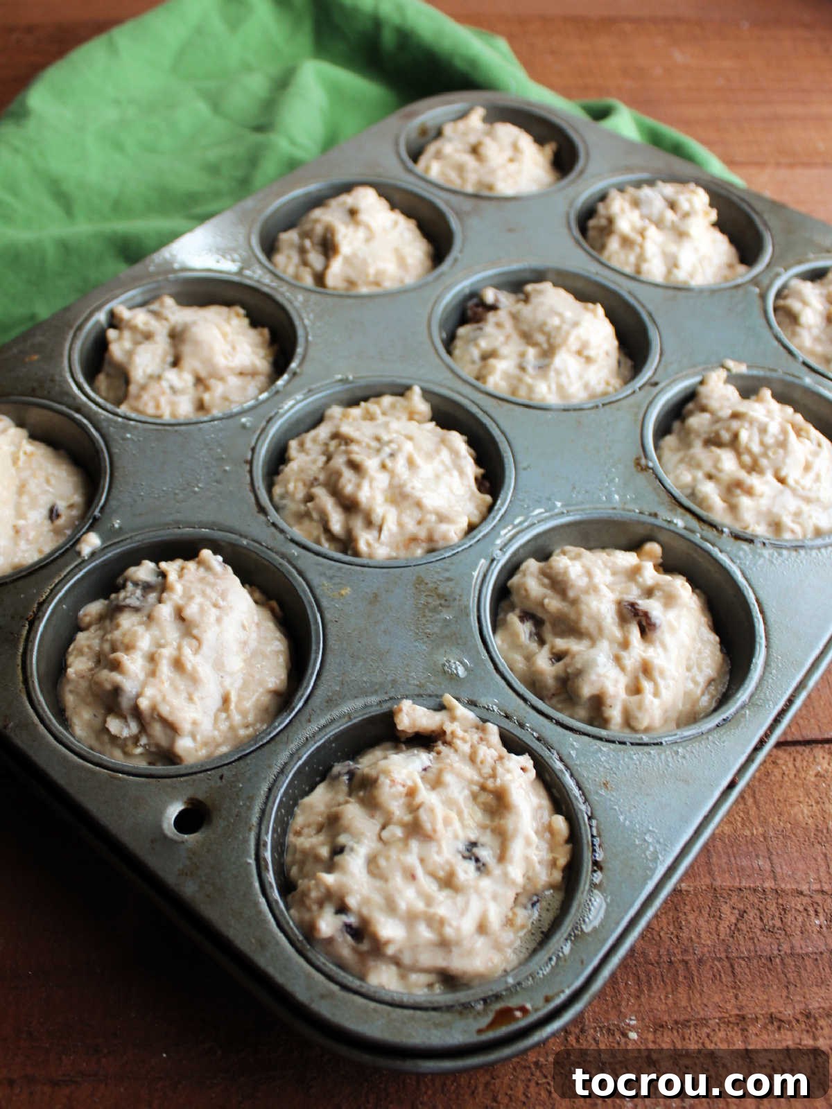 A muffin pan filled with perfectly portioned oatmeal sourdough muffin batter, poised to be baked to golden perfection.