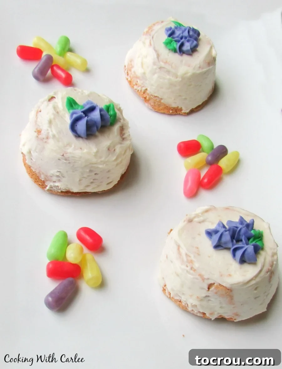 Upside Down Angel Food Cupcakes with Frosting Mini angel food cakes with white frosting and purple frosting flowers on top, surrounded by bright colored candies on a white surface.