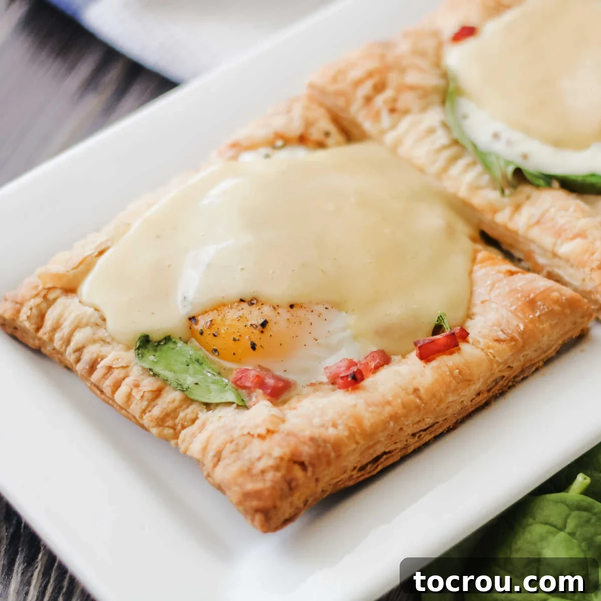 Golden puff pastry eggs benedict tart with fresh spinach, savory ham, and a luscious hollandaise sauce, ready to be enjoyed.