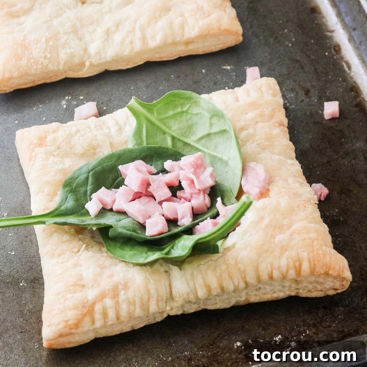 Fresh spinach and savory ham slices arranged neatly on a square of golden puff pastry, ready for the egg.