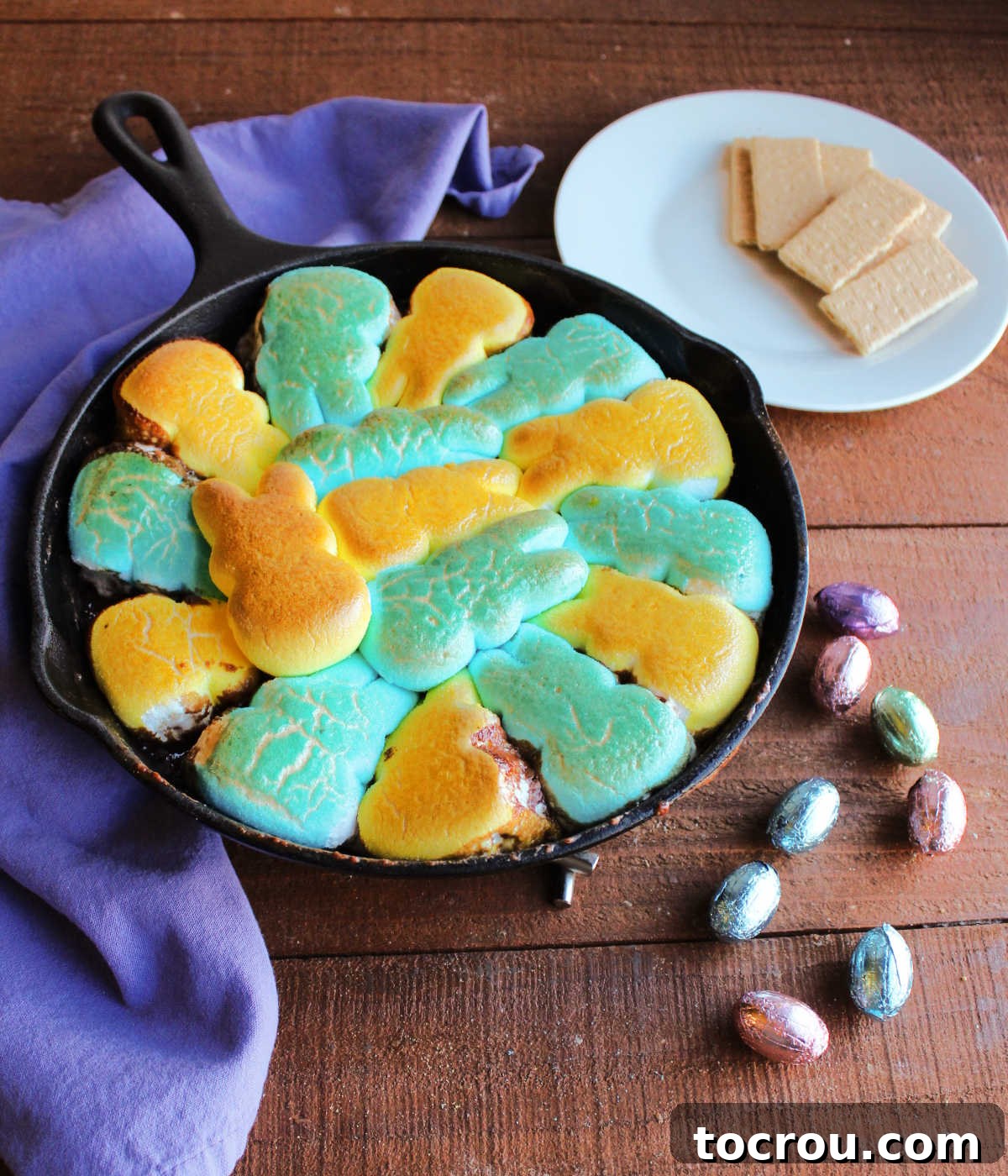 Freshly Broiled Peeps S'mores Dip Cast iron skillet filled with Peep smore dip fresh from the oven, the marshmallows are puffed and golden brown with a plate of graham crackers in the background waiting to be dipped.