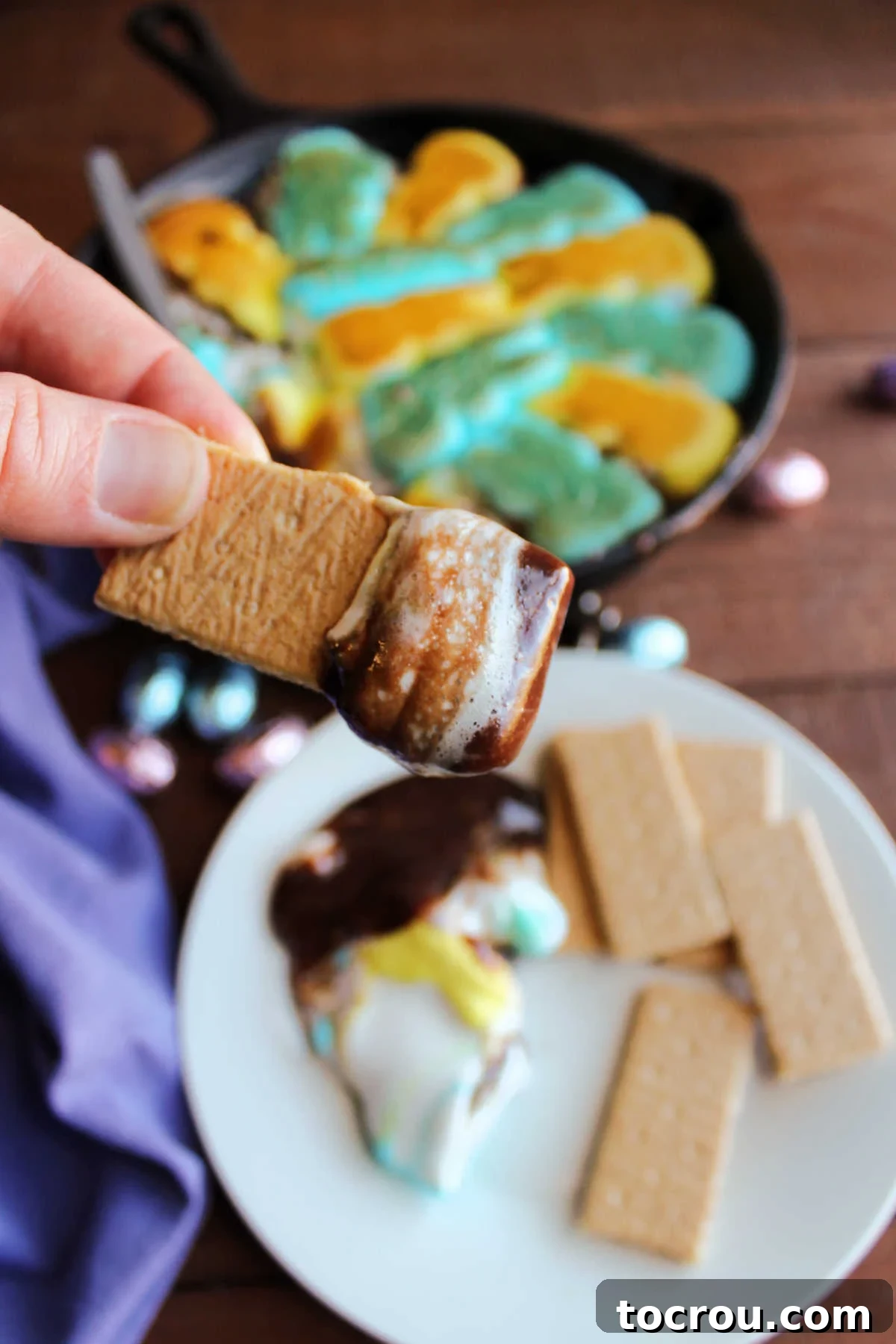 Close-up of Gooey Peeps S'mores Dip Graham cracker dipped in peeps smore dip showing gooey marshmallow and melted chocolate.