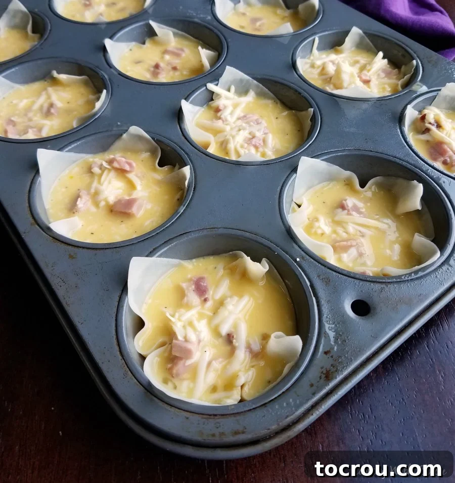 Wonton wrappers in muffin tin Muffin tin lined with delicate wonton wrappers, ready to be filled with the savory egg, ham, and cheese mixture before baking.