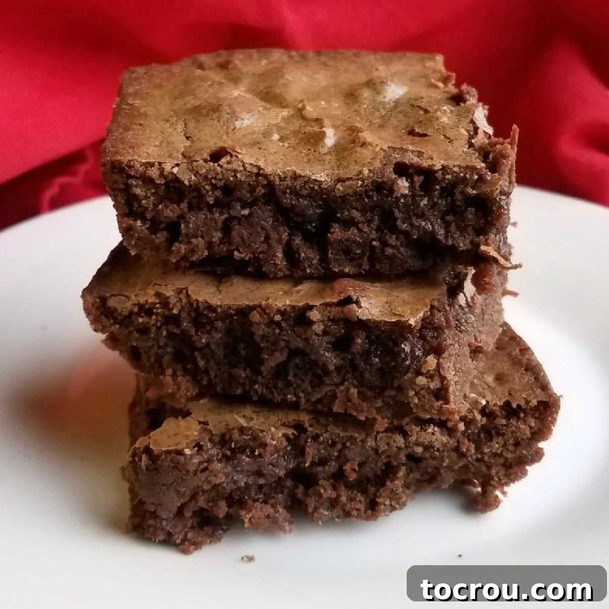 Stack of rich, fudgy brownies with beautifully crackled tops, showcasing their irresistible texture.