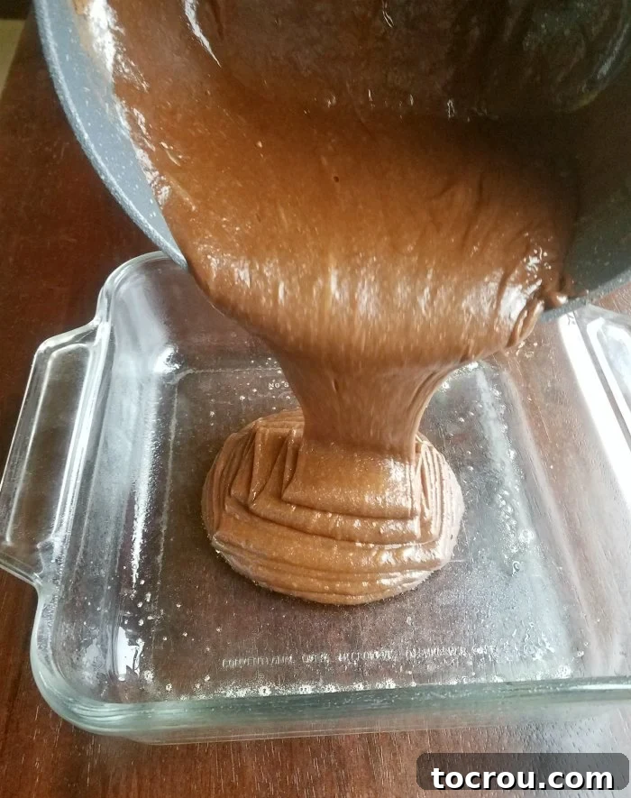 Thick, dark brownie batter being poured into a greased baking pan, ready for the oven.