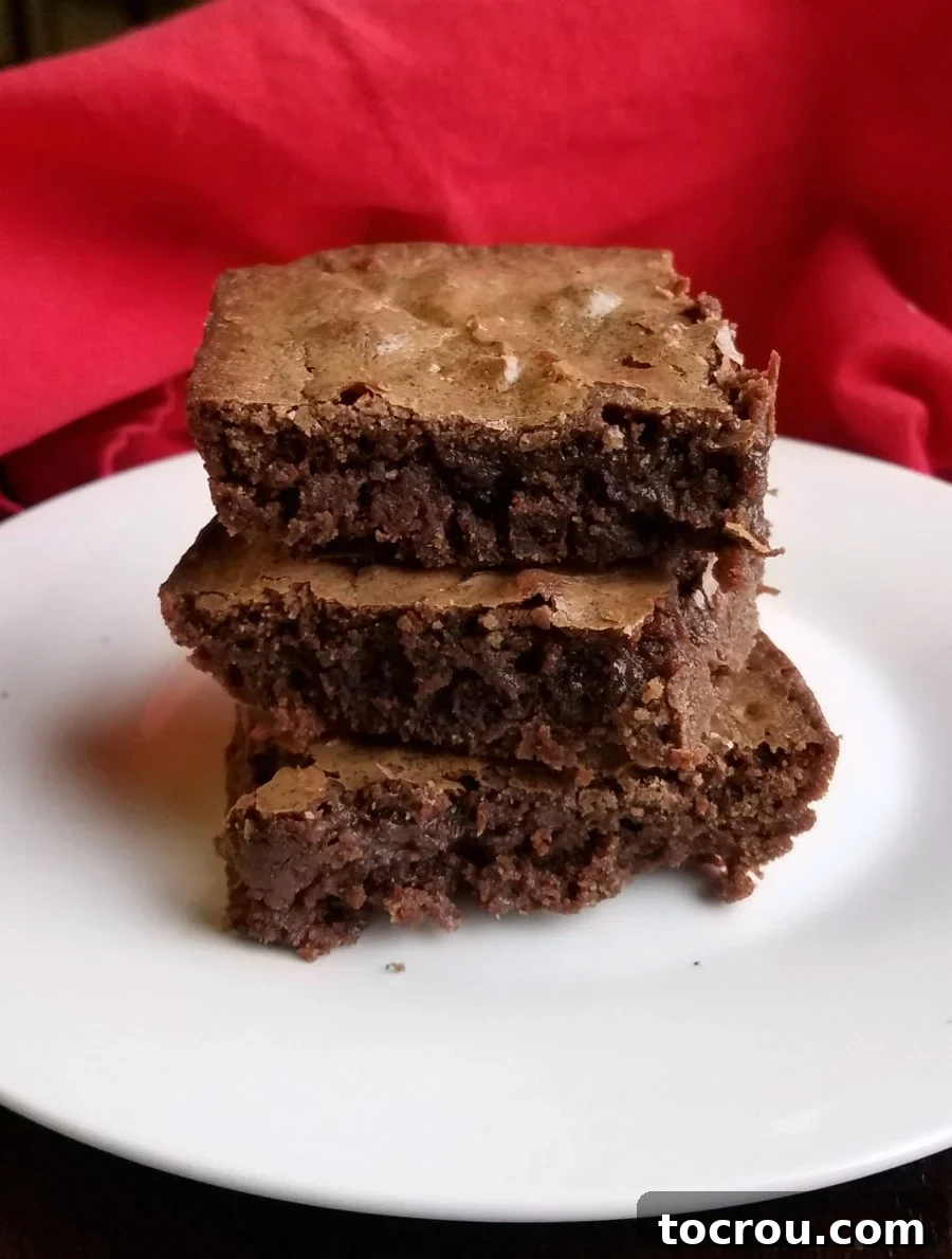A stack of three decadent chocolate fudgy brownies on a white plate, ready to be enjoyed.