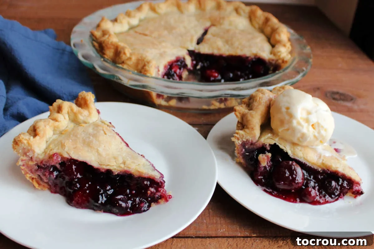 Two slices of cherry berry pie with thick filling made of raspberries, cherries, blueberries and more in flaky crust with pie plate nearby.