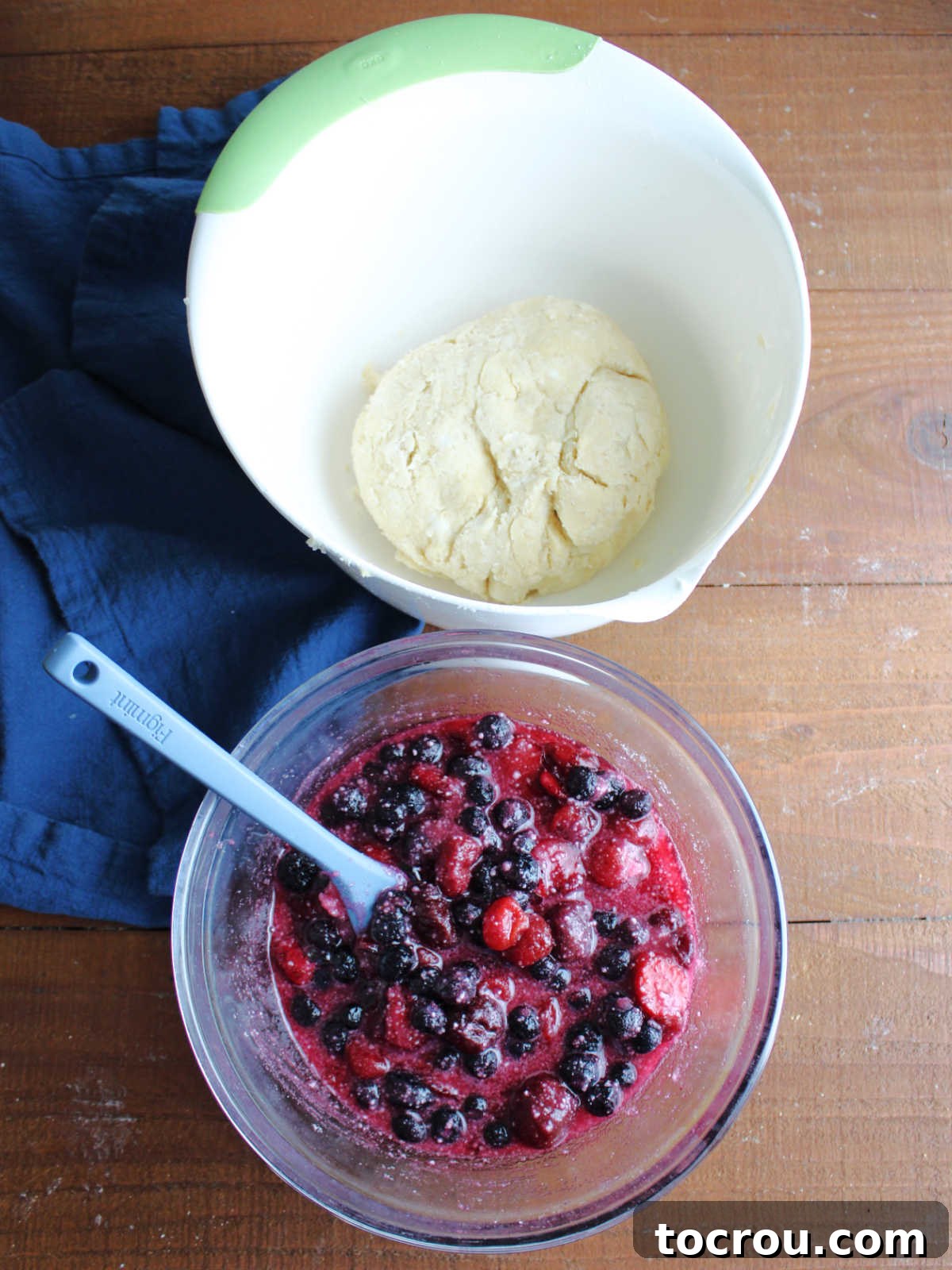 Bowl of mixed berries and cherries with sugar and instant tapioca next to a bowl with pie pastry inside.