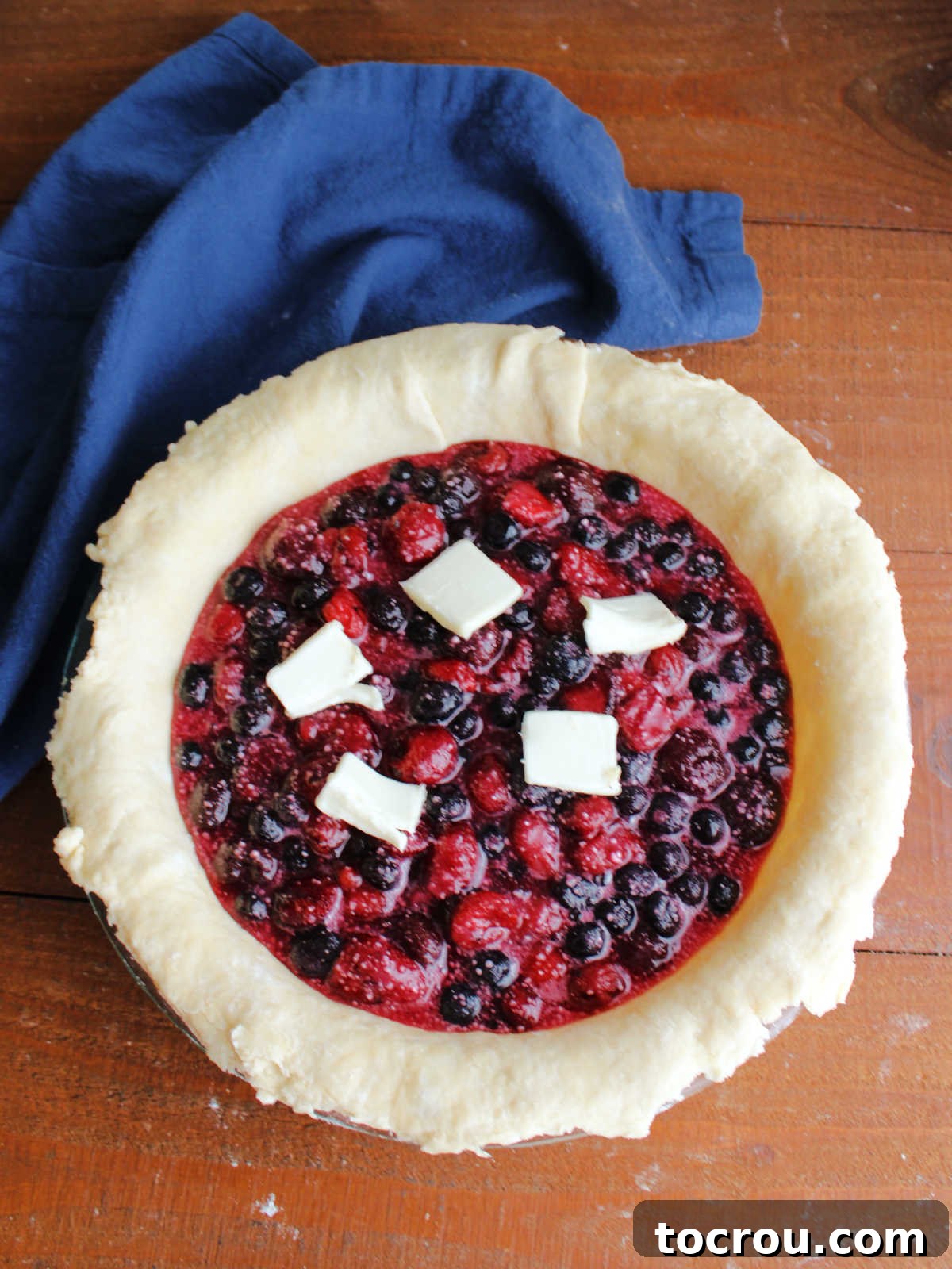 Pie plate filled with pie pastry and cherry berry filling dotted with some butter, ready for the top crust.