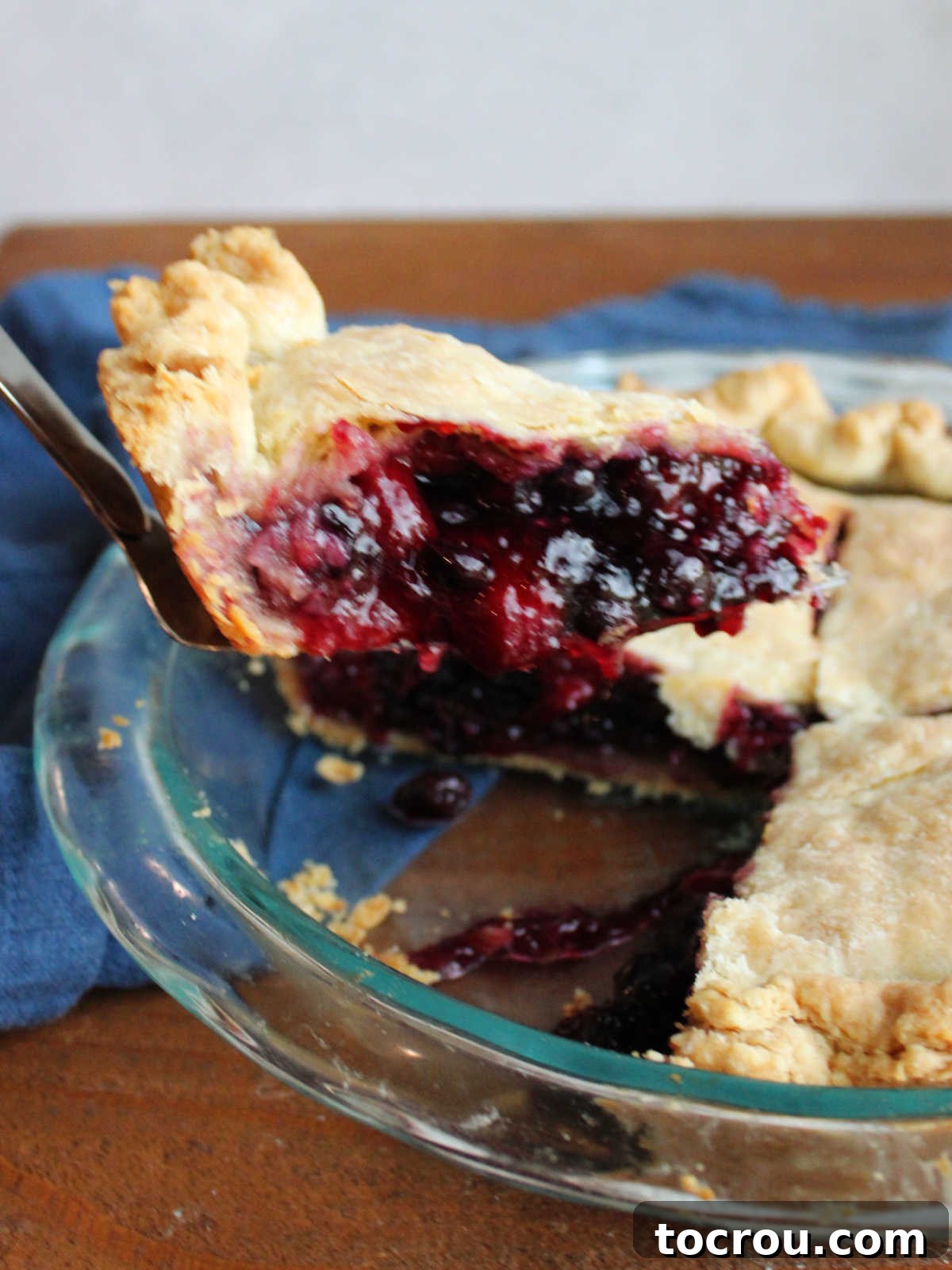 Spatula lifting slice of cherry berry pie out of the pie plate showing thick filling with lots of berries inside.