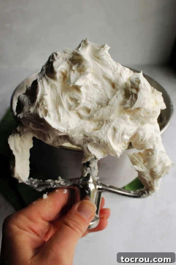 Close-up of a mixer paddle laden with freshly made white buttercream frosting, highlighting its light and airy texture.